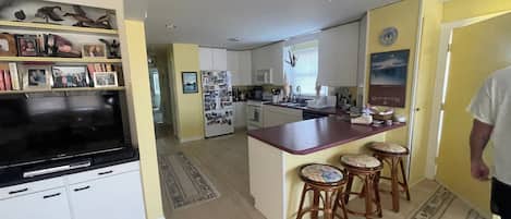 A kitchen with a central island, bar stools, a refrigerator with photos, and a television on a stand.