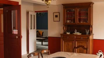 Uma sala de jantar com um lustre, cadeiras de madeira, uma mesa com toalha branca e um aparador de madeira com portas de vidro.