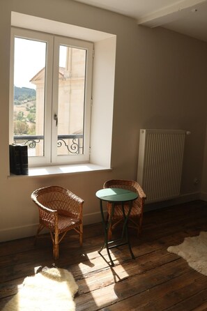 Una habitación con ventana, dos sillones de mimbre, una mesita redonda y un radiador.