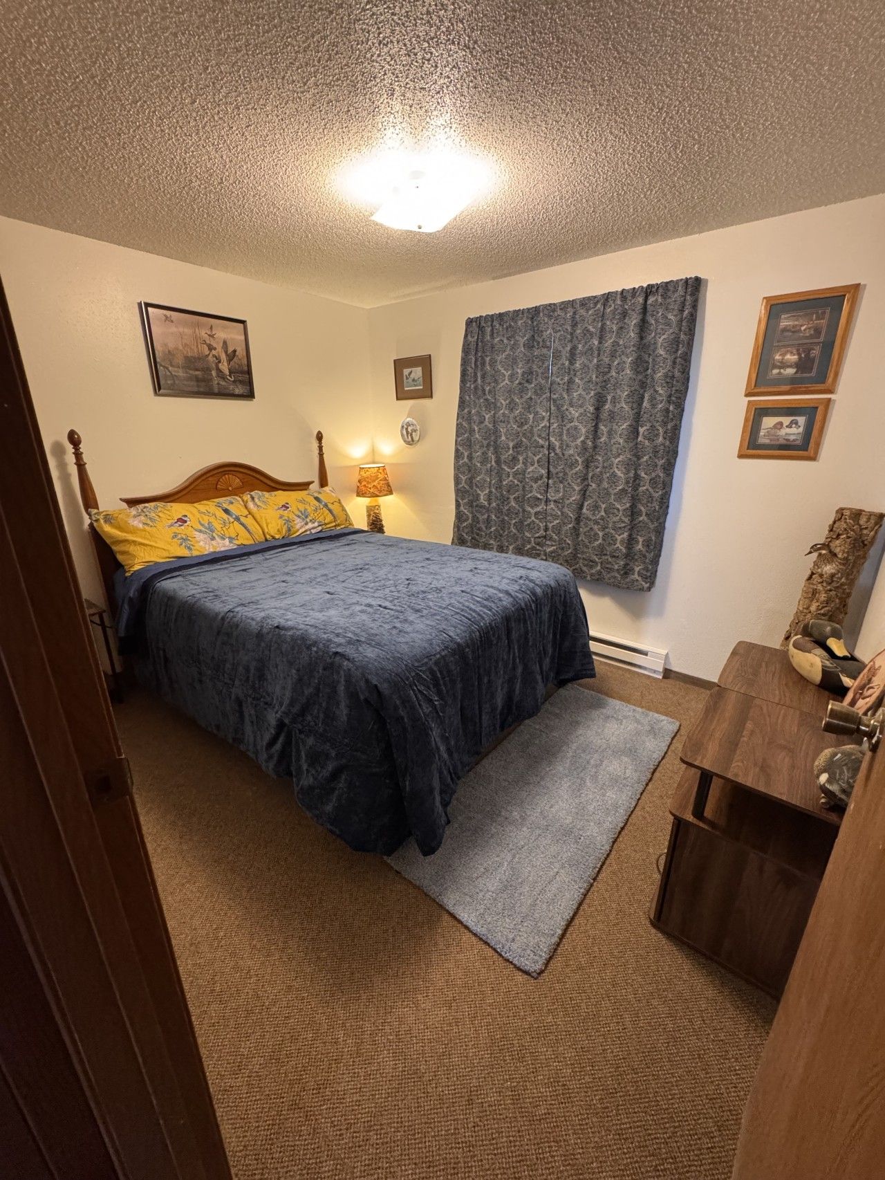 A bedroom with a bed, a nightstand, a lamp, a window with curtains, and a dresser.
