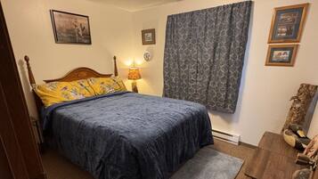 A bedroom with a bed, a nightstand, a lamp, a window with curtains, and a dresser.