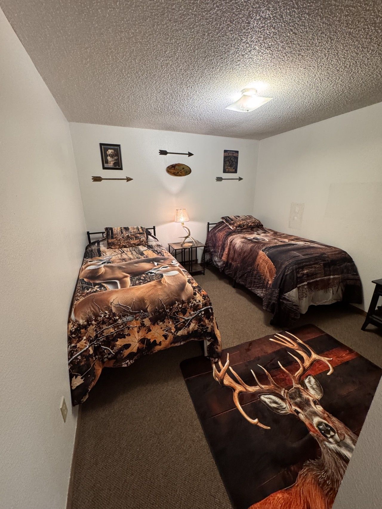 Une chambre avec deux lits, une table de chevet, une lampe et un tapis décoré de motifs de cerfs.