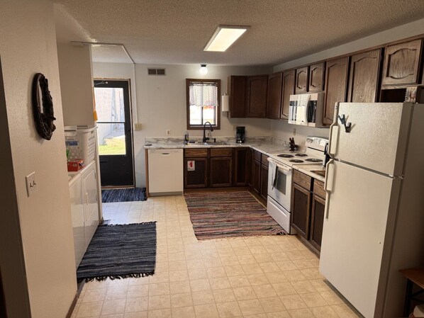 A compact kitchen with a refrigerator, stove, sink, and wooden cabinets.