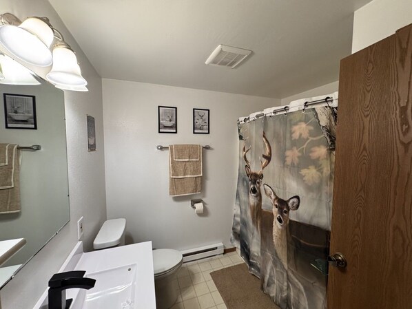 A bathroom with a toilet, sink, and shower curtain with a deer design.