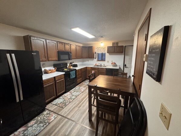 A compact kitchen with wooden cabinets, a black refrigerator, a microwave, and a dining table with chairs.