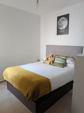 Ein ordentlich bezogenes Bett mit einer senffarbenen Decke, einem grauen Kopfteil und einem Wandbild mit dem Mond.
