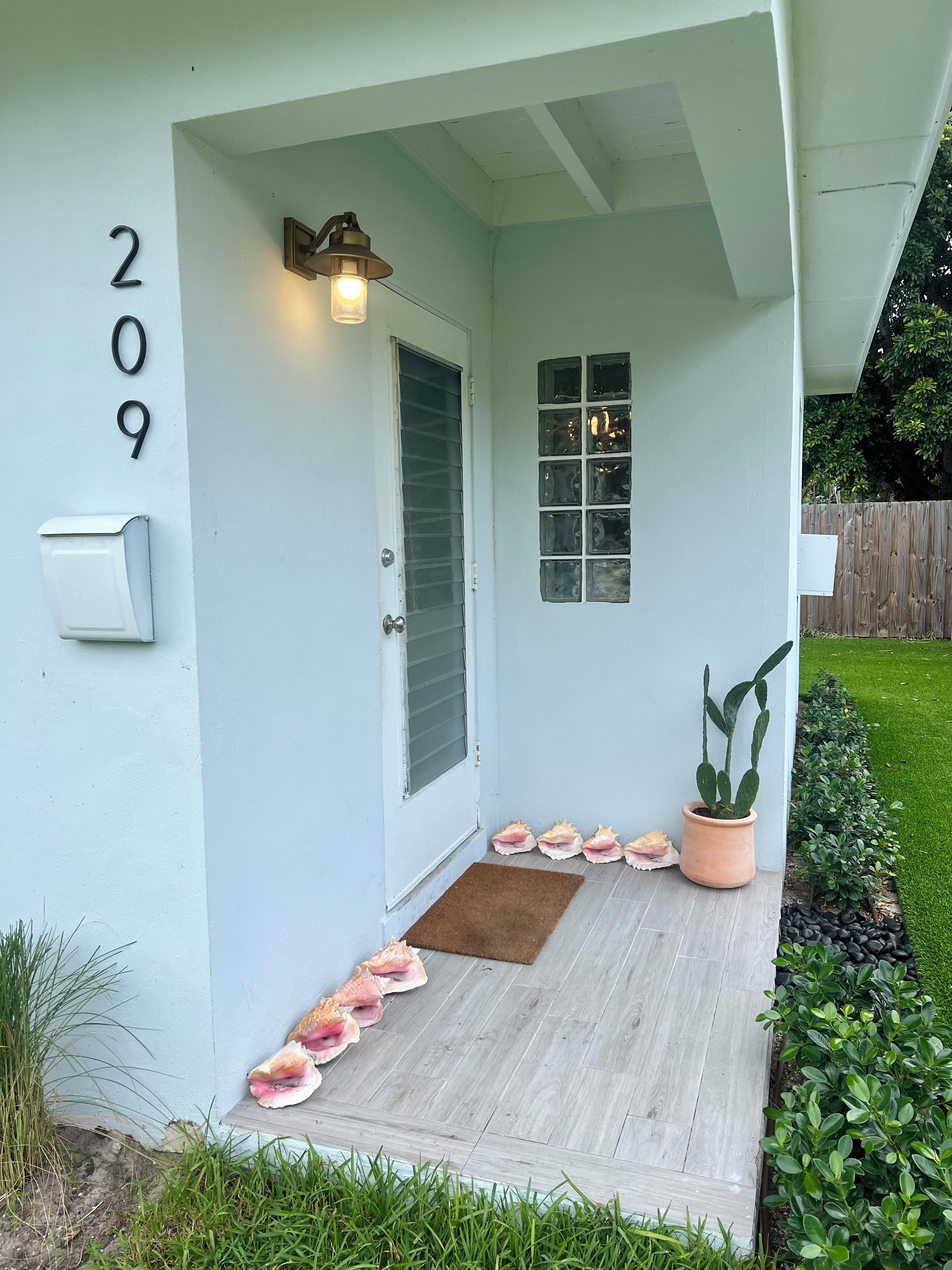 Una casa con el número 209 en la pared, una puerta principal, una ventana, un porche con un felpudo marrón y una planta en maceta.