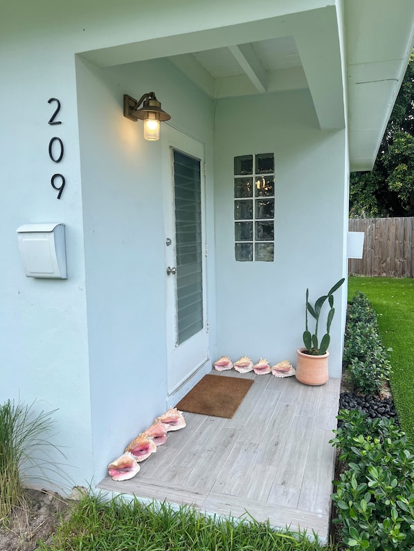 Una casa con el número 209 en la pared, una puerta principal, una ventana, un porche con un felpudo marrón y una planta en maceta.