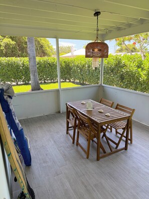 A covered patio with a wooden table and chairs, a hanging light fixture, and a view of a well-maintained garden.