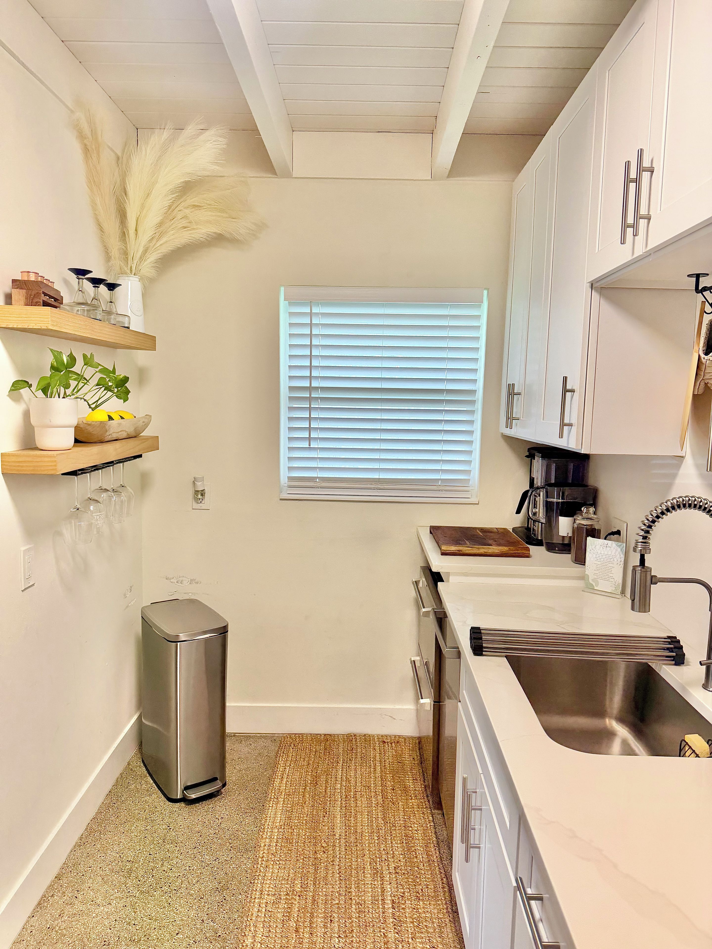 Una cocina con armarios blancos, un lavamanos de acero inoxidable y una ventana con persianas.