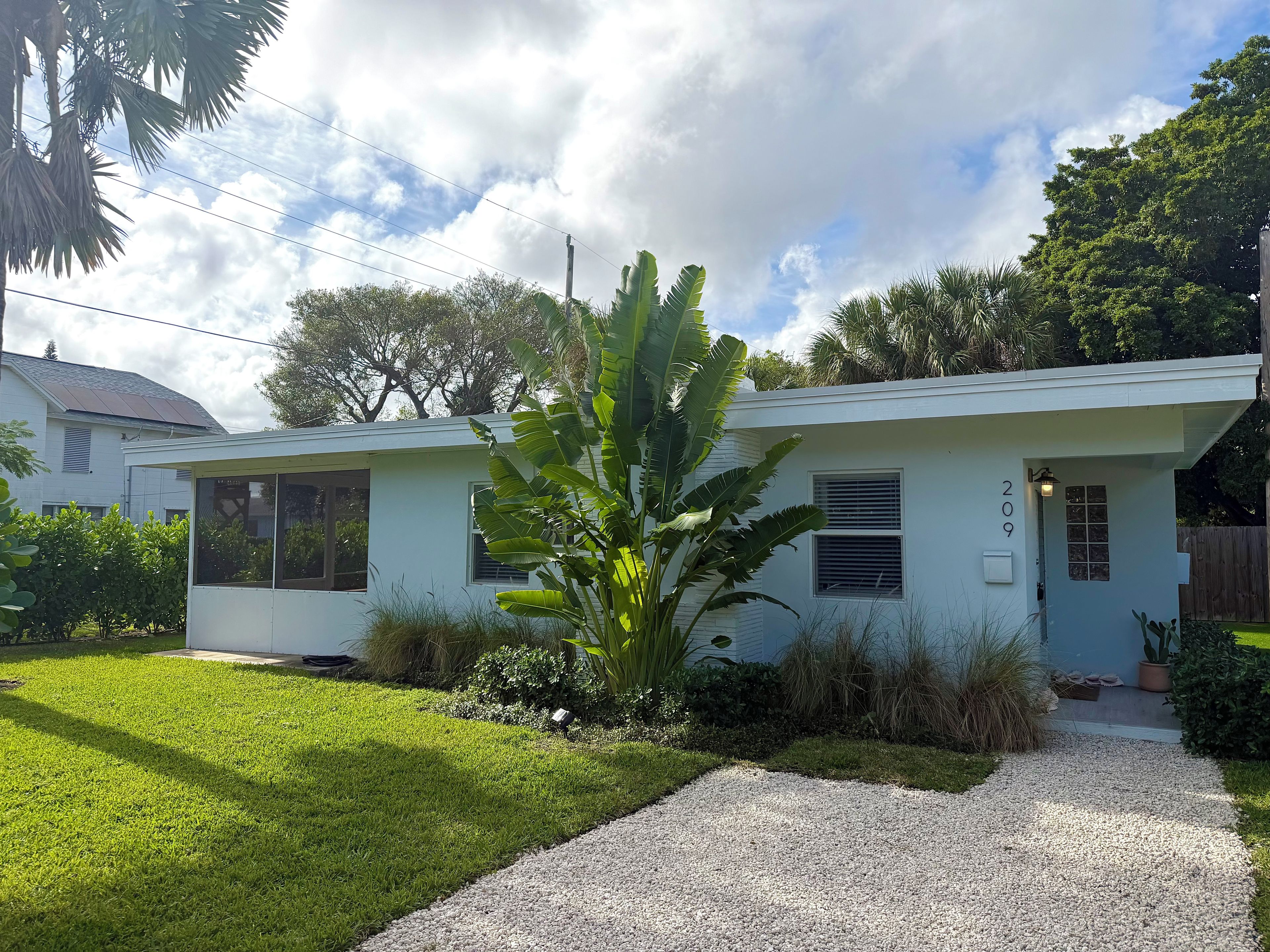 A single-story house with a white exterior, a front porch, and a gravel driveway.