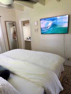 A bedroom with a large bed, a television on the wall, and a closet with hanging items. - The Surf Shack - Minutes from Beach and Atlantic Ave (Boynton Beach)