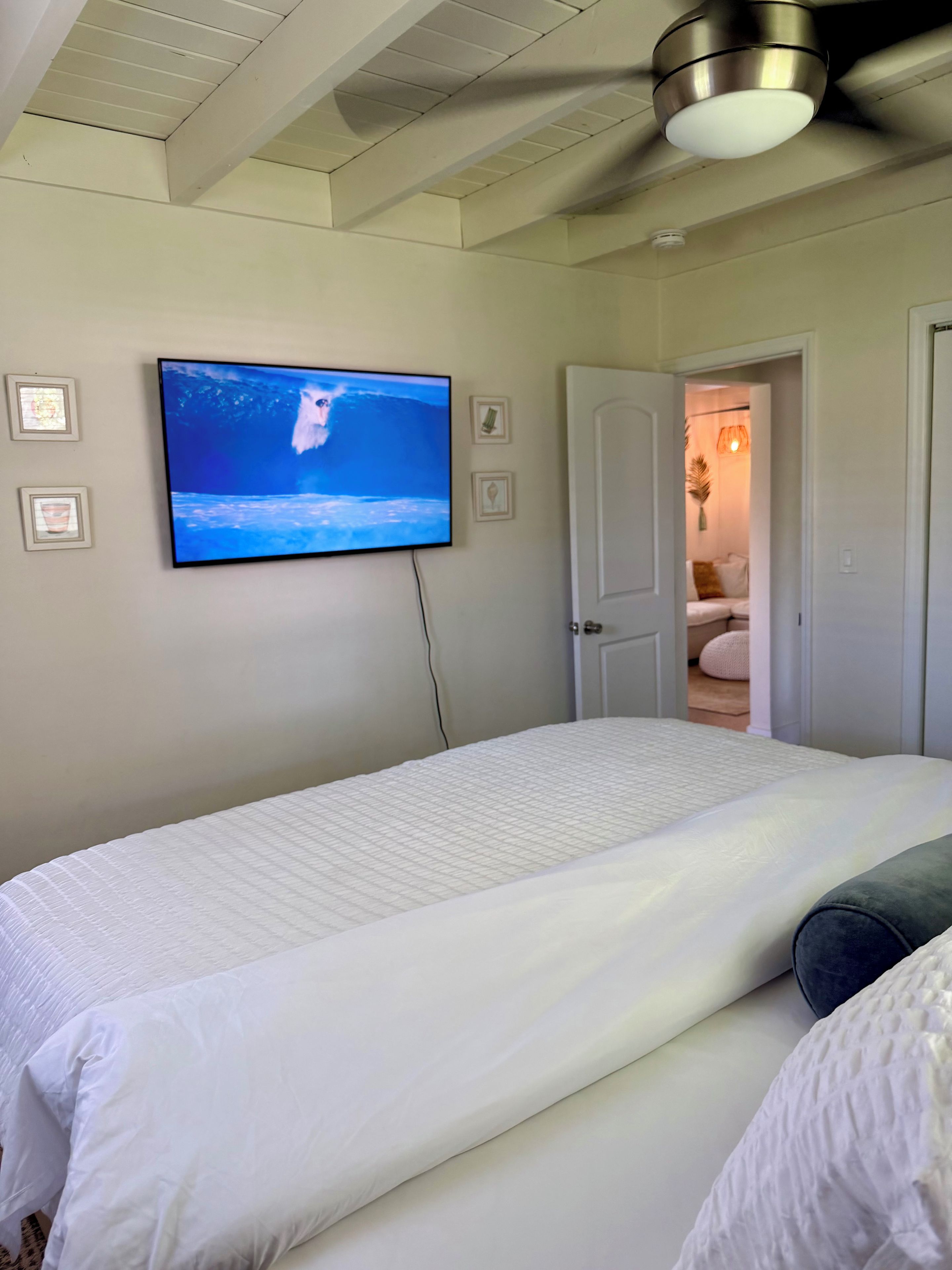 Un dormitorio con cama, televisión montada en la pared y ventilador de techo.