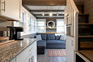 A modern kitchen with a built-in oven, a coffee machine, and a granite countertop. - DC57: Shell Yeah | Tiny Home | Centrally Located on Back Road (Ocracoke)
