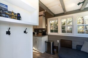 Eine kompakte Küche mit einer Kaffeemaschine, einem Mülleimer und einem Fenster mit Blick auf Bäume.