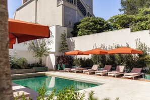 A poolside area with lounge chairs and umbrellas, surrounded by greenery and a building with patterned tiles. - Premium Studio Suite - Vila Catarina Luxury Apartments (Porto)