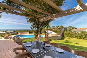 Un espace extérieur aménagé pour les repas, avec une piscine, des chaises et une pergola.