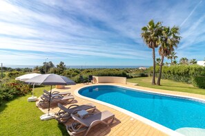 A swimming pool with lounge chairs and umbrellas, surrounded by greenery and palm trees. - Casa Carpe Diem - 5 Bed Villa With Panoramic Sea Views & Private Pool (Carvoeiro)