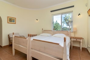A bedroom with a double bed, a chair, a bedside table, a nightstand, a window with a view of palm trees, and a wall-mounted light fixture. - Casa Carpe Diem - 5 Bed Villa With Panoramic Sea Views & Private Pool (Carvoeiro)