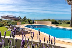 Une piscine entourée de verdure, avec des chaises longues et un parasol, offrant une vue sur la mer.