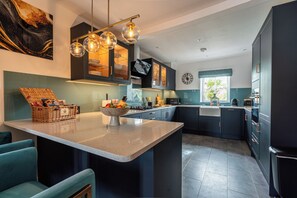 A modern kitchen with a central island, dark cabinetry, and a hanging light fixture. - Luxury Loft Above The Chipping Steps, Tetbury  (Tetbury)