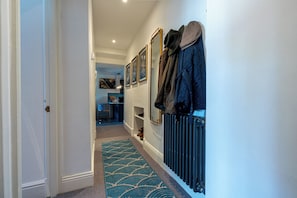 Un couloir avec un radiateur, une moquette bleue et un porte-manteau avec des chapeaux.