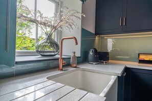 Une cuisine moderne avec une grande fenêtre, un robinet en cuivre, un vase décoré de branches et une machine à café.