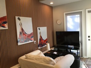 A modern living room with a flat-screen TV, a sofa, and two abstract paintings on the wall. - Your Peaceful Durham Getaway – Near Duke, UNC & RTP (Durham)