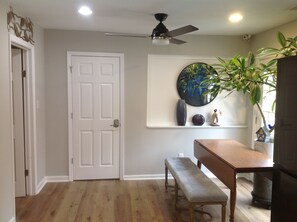A room with a white door, a ceiling fan, a round wall art piece, a bench, and a table. - Your Peaceful Durham Getaway – Near Duke, UNC & RTP (Durham)