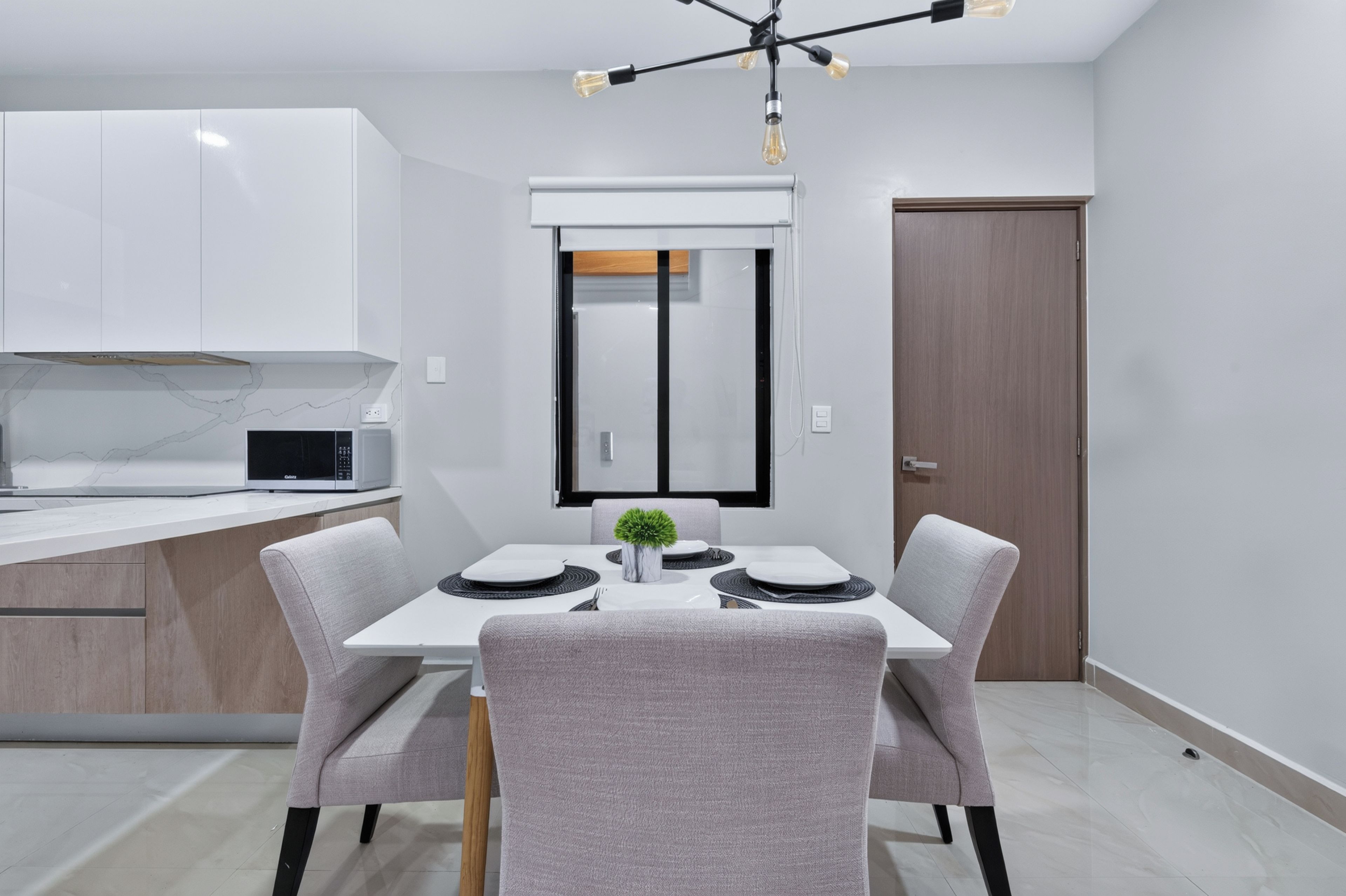 Una cocina moderna con armarios blancos, un microondas y un comedor con una mesa dispuesta para dos.