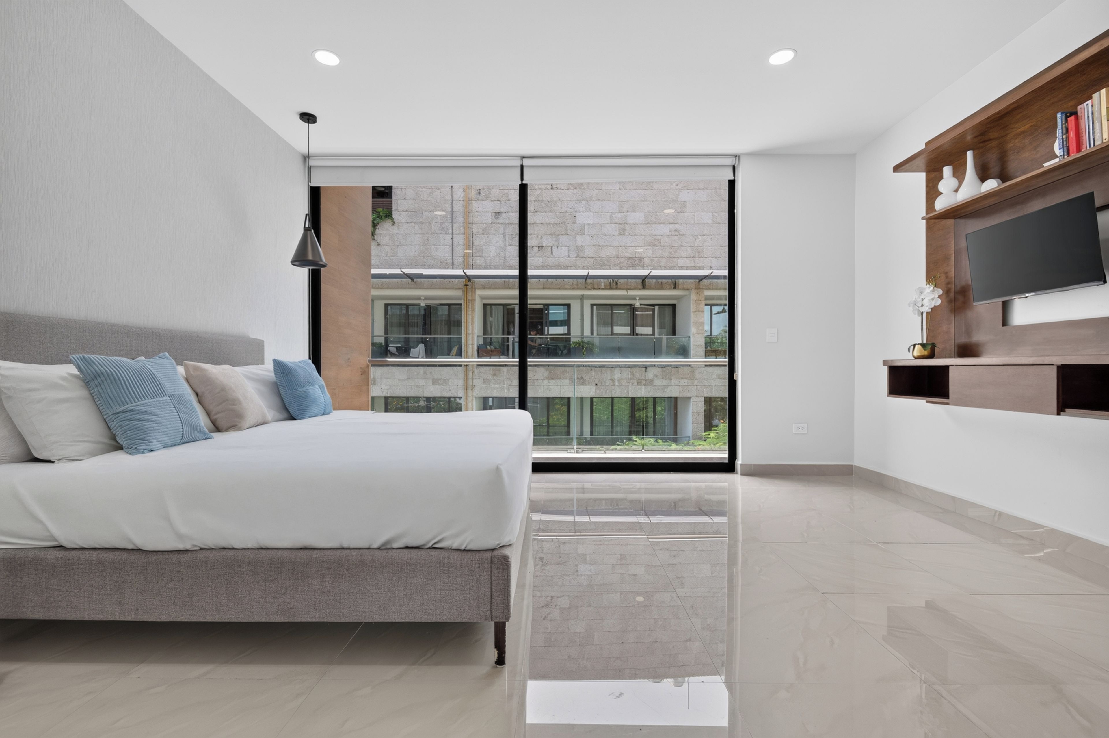 Een moderne slaapkamer met een bed, een televisie en een balkon met uitzicht op een gebouw.