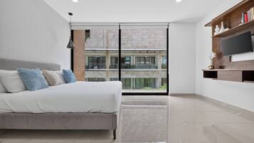 Een moderne slaapkamer met een bed, een televisie en een balkon met uitzicht op een gebouw.