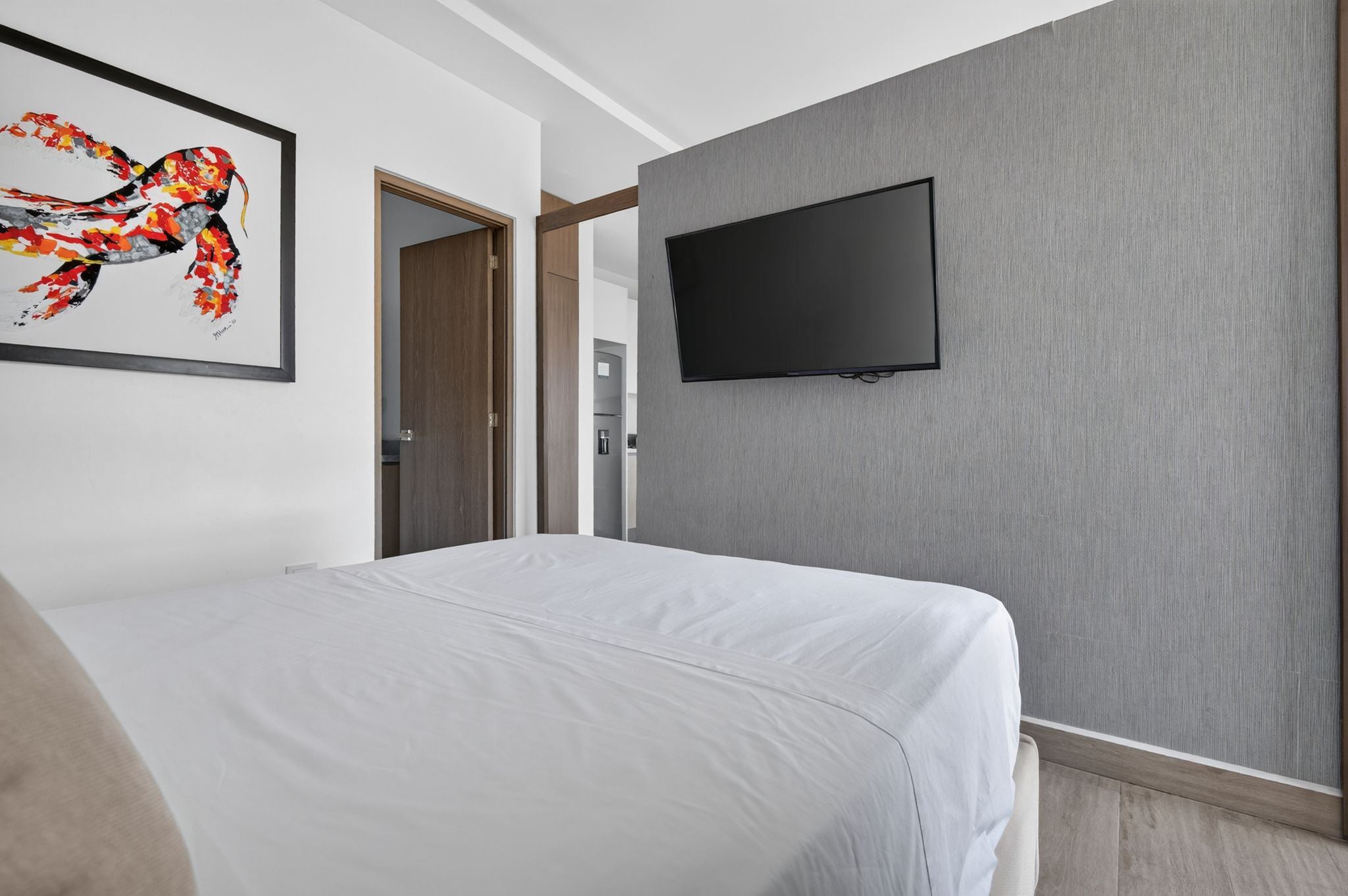 Habitación de hotel con una cama, un televisor de pantalla plana en la pared y una puerta que da al baño.