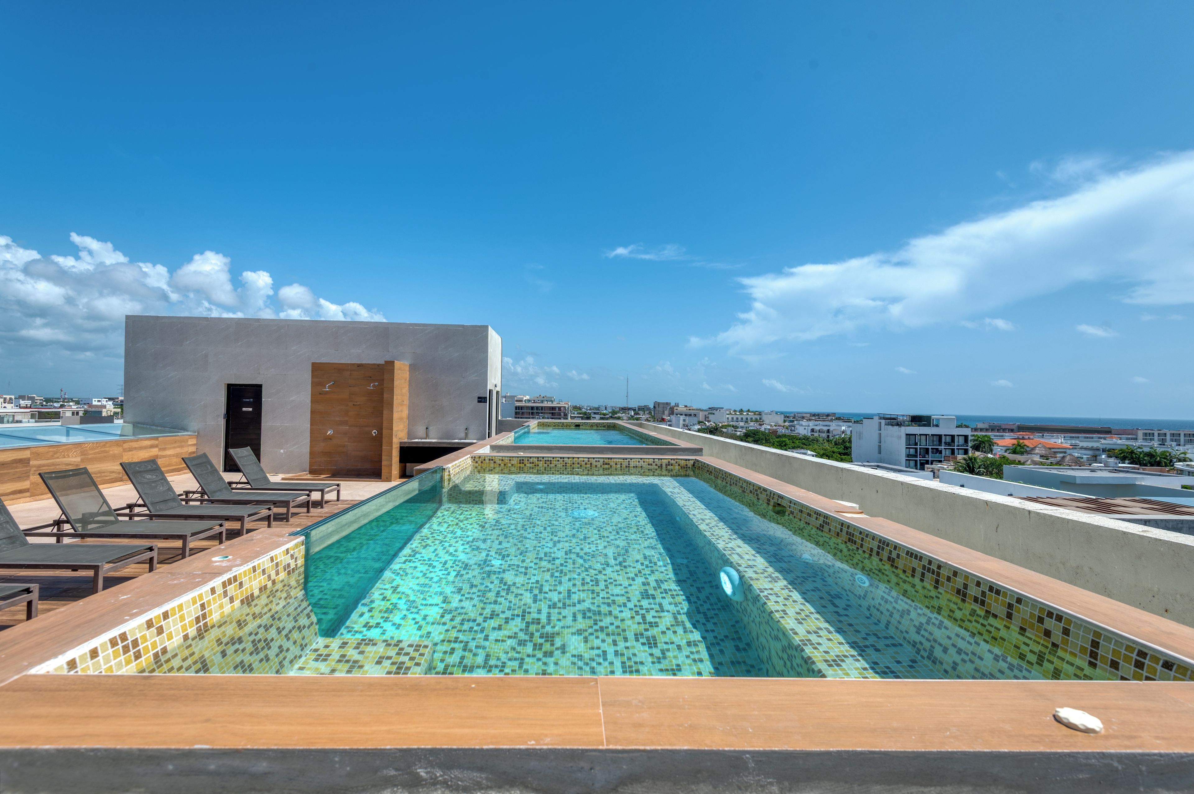 Una piscina en la azotea con agua azul cristalina, sillas de descanso y vistas a la ciudad y al océano.