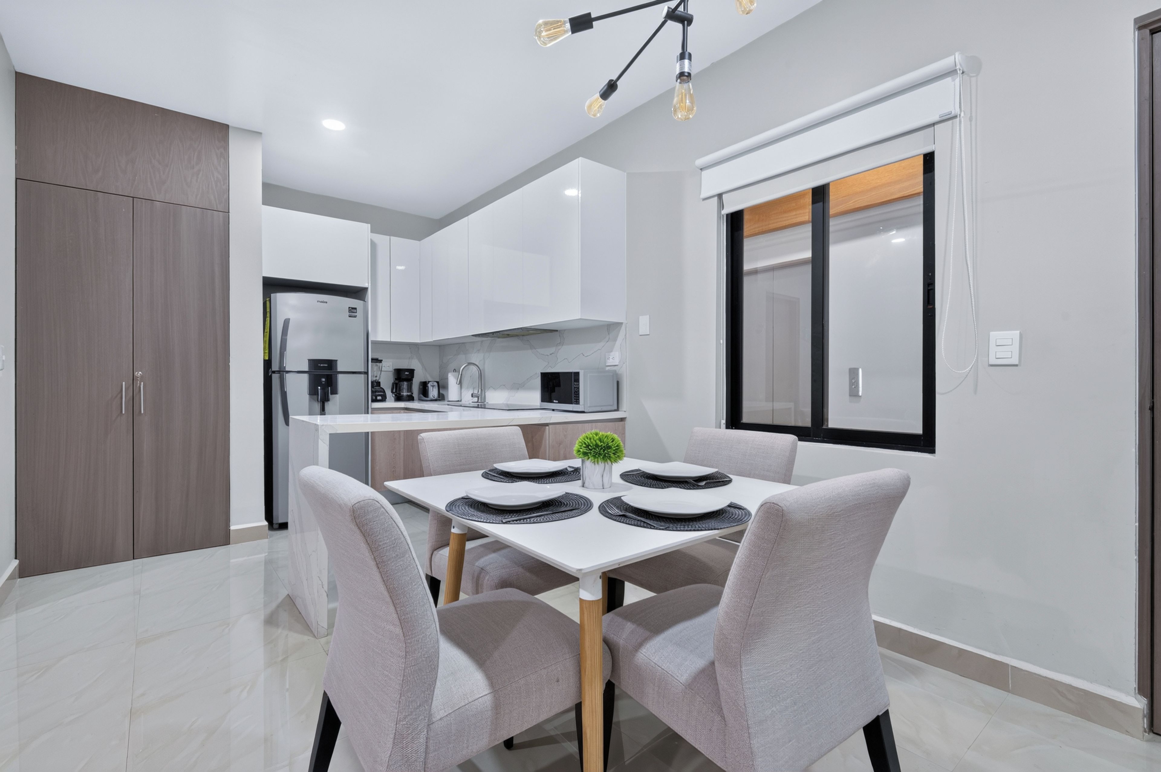 A modern kitchen with white cabinets, a built-in oven, and a dining area with a table set for four.
