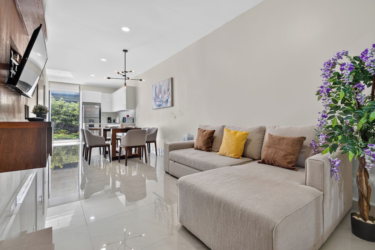 Uma sala de estar moderna com sofá, área de jantar e cozinha ao fundo.