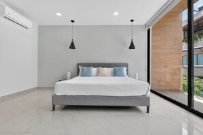 Un dormitorio moderno con una cama grande, dos lámparas colgantes y vistas a la vegetación exterior.