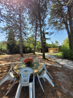 A round table with a patterned tablecloth and white plastic chairs, surrounded by trees and a clear sky. - House with a yard in a quiet neighborhood (Entraigues-sur-la-Sorgue)