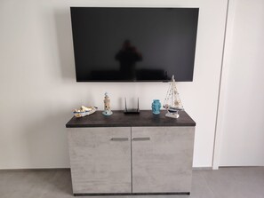 A flat-screen TV mounted on a wall above a grey cabinet with decorative items on top. - Marina di Ragusa Waterfront - Charming, Modern Oceanfront Apartment (Marina di Ragusa)