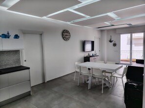 A modern kitchen with white cabinets, a black countertop, and a dining area with a white table and chairs. - Marina di Ragusa Waterfront - Charming, Modern Oceanfront Apartment (Marina di Ragusa)