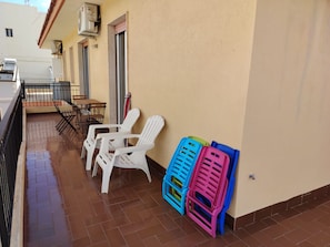 A balcony with white plastic chairs and tables, a tiled floor, and a wall-mounted air conditioner. - Marina di Ragusa Waterfront - Charming, Modern Oceanfront Apartment (Marina di Ragusa)