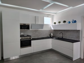 A modern kitchen with white cabinetry, a black countertop, a built-in oven, a microwave, a sink, and a window. - Marina di Ragusa Waterfront - Charming, Modern Oceanfront Apartment (Marina di Ragusa)