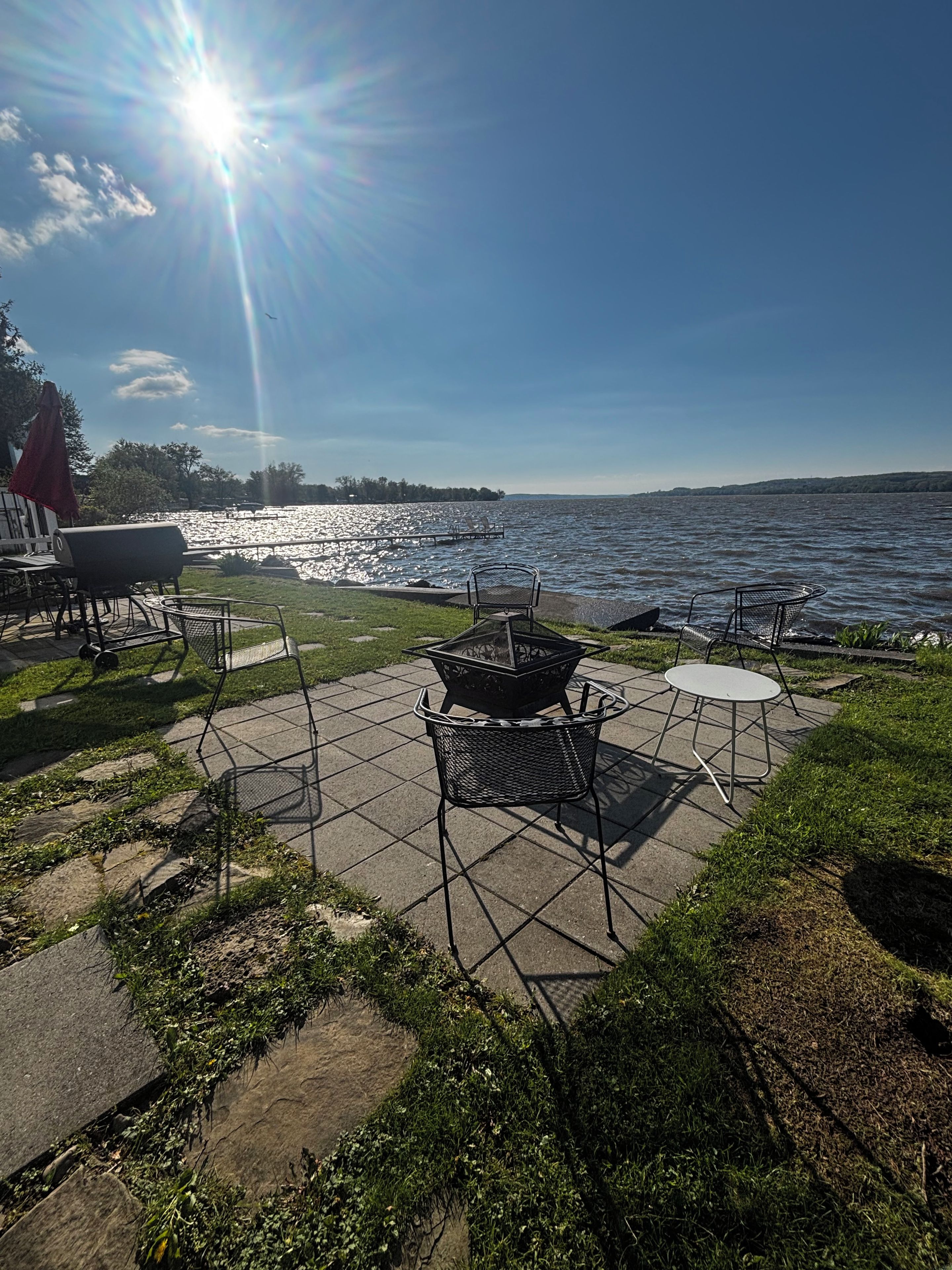 Eine Terrasse im Freien mit Feuerstelle, Sitzgelegenheiten und Blick auf einen See.