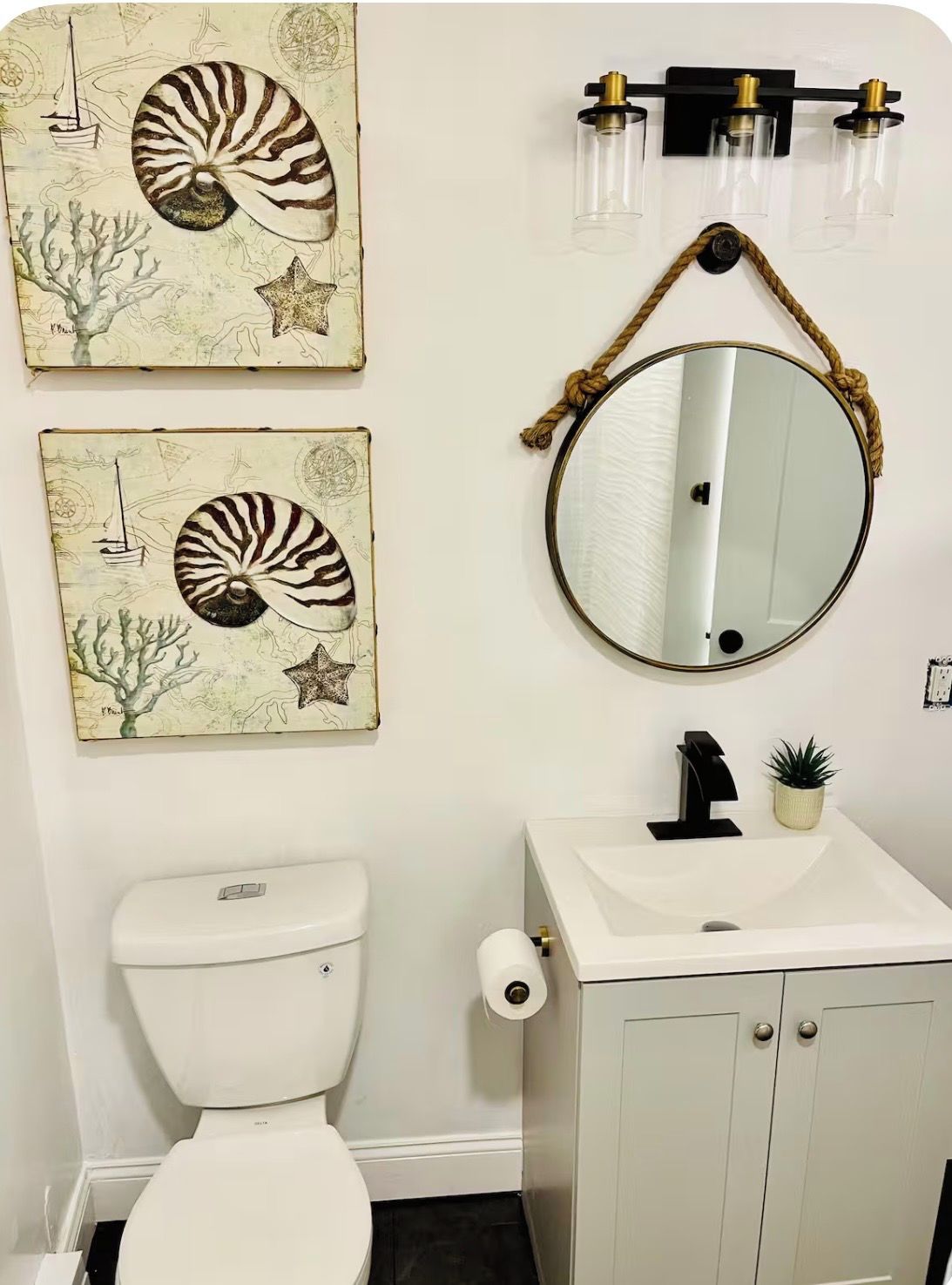 Une salle de bain équipée de toilettes, d’un lavabo et de deux œuvres d’art fixées au mur, représentant des coquillages et une étoile de mer.