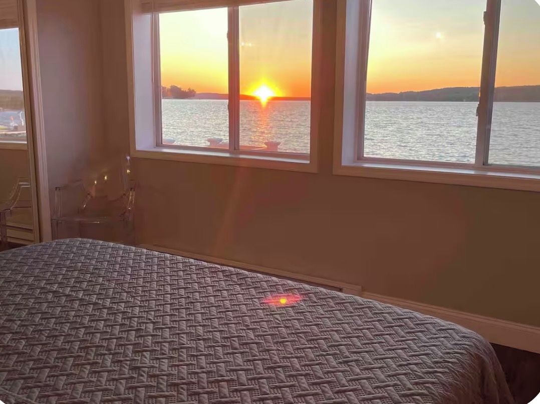 Ein Zimmer mit einem Bett und Blick auf einen Sonnenuntergang über dem Wasser durch ein Fenster.