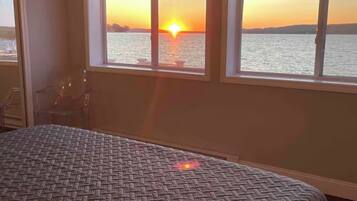 Ein Zimmer mit einem Bett und Blick auf einen Sonnenuntergang über dem Wasser durch ein Fenster.