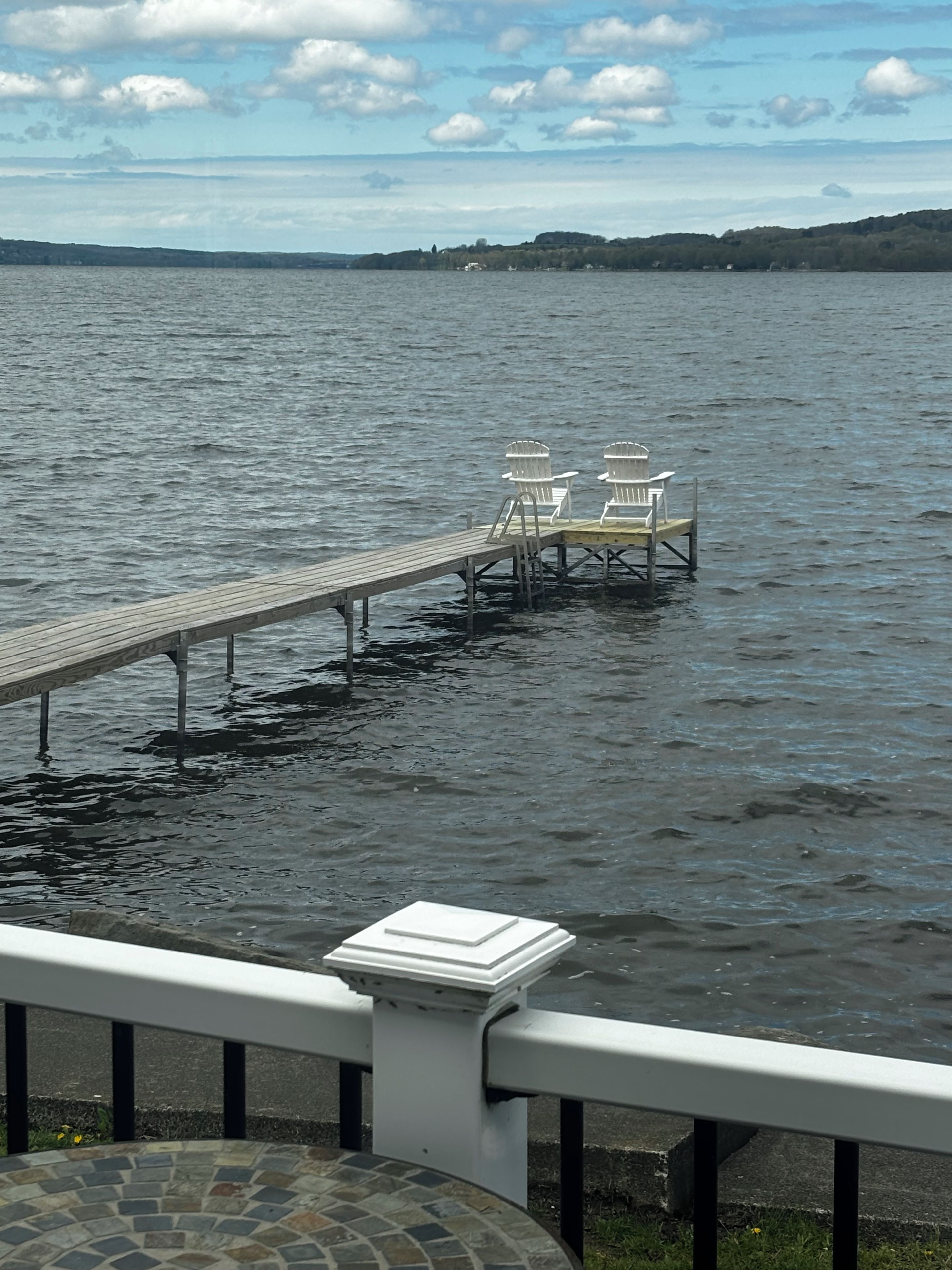 En träbrygga som sträcker sig ut i en sjö, med två Adirondack-stolar placerade på bryggan.