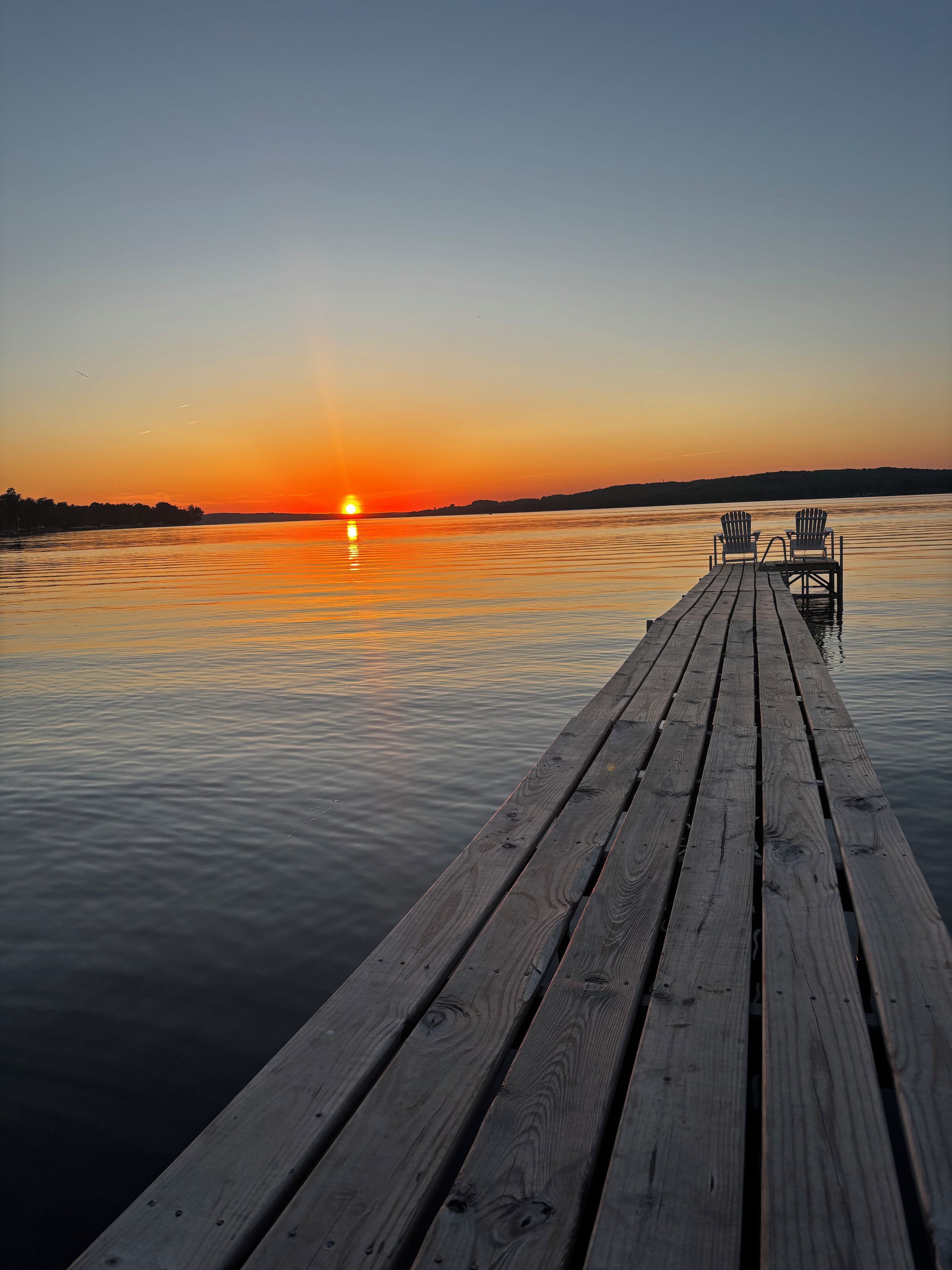 Une jetée en bois s’étendant sur une étendue d’eau calme, avec un coucher de soleil en arrière-plan.