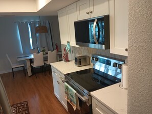 Une cuisine de taille réduite avec des meubles blancs, une cuisinière noire et un four à micro-ondes.
