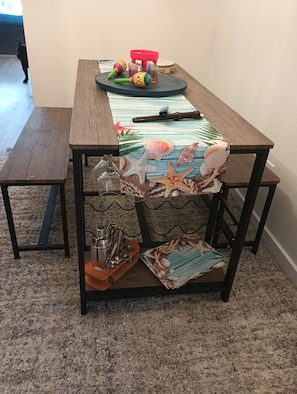 Une table à manger avec un plateau en bois, une chaise rouge et une nappe à motifs de plage.